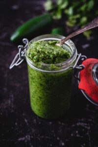 Green pesto in a jar with a spoon.