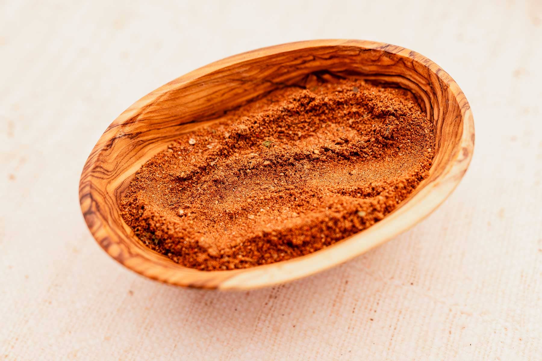 A shallow wooden bowl filled with Baharat Spice Mix.