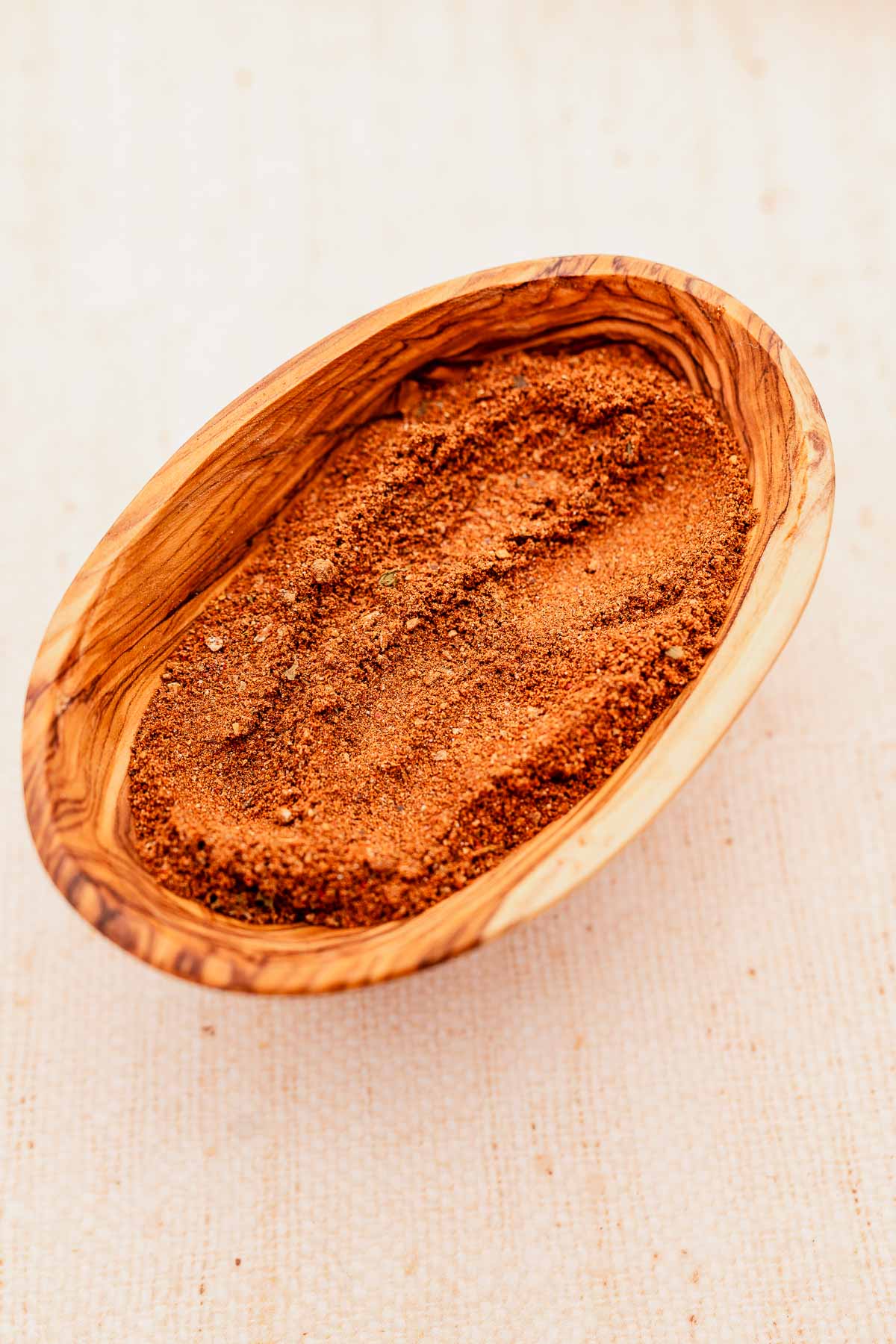 A wooden bowl filled with baharat, a brown powder.