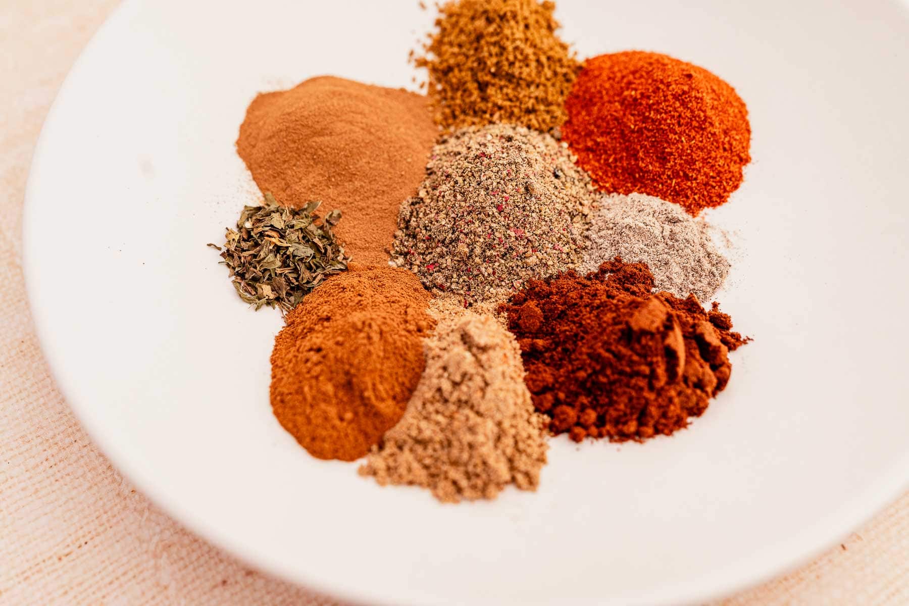 Baharat spices in a white plate on a wooden table.