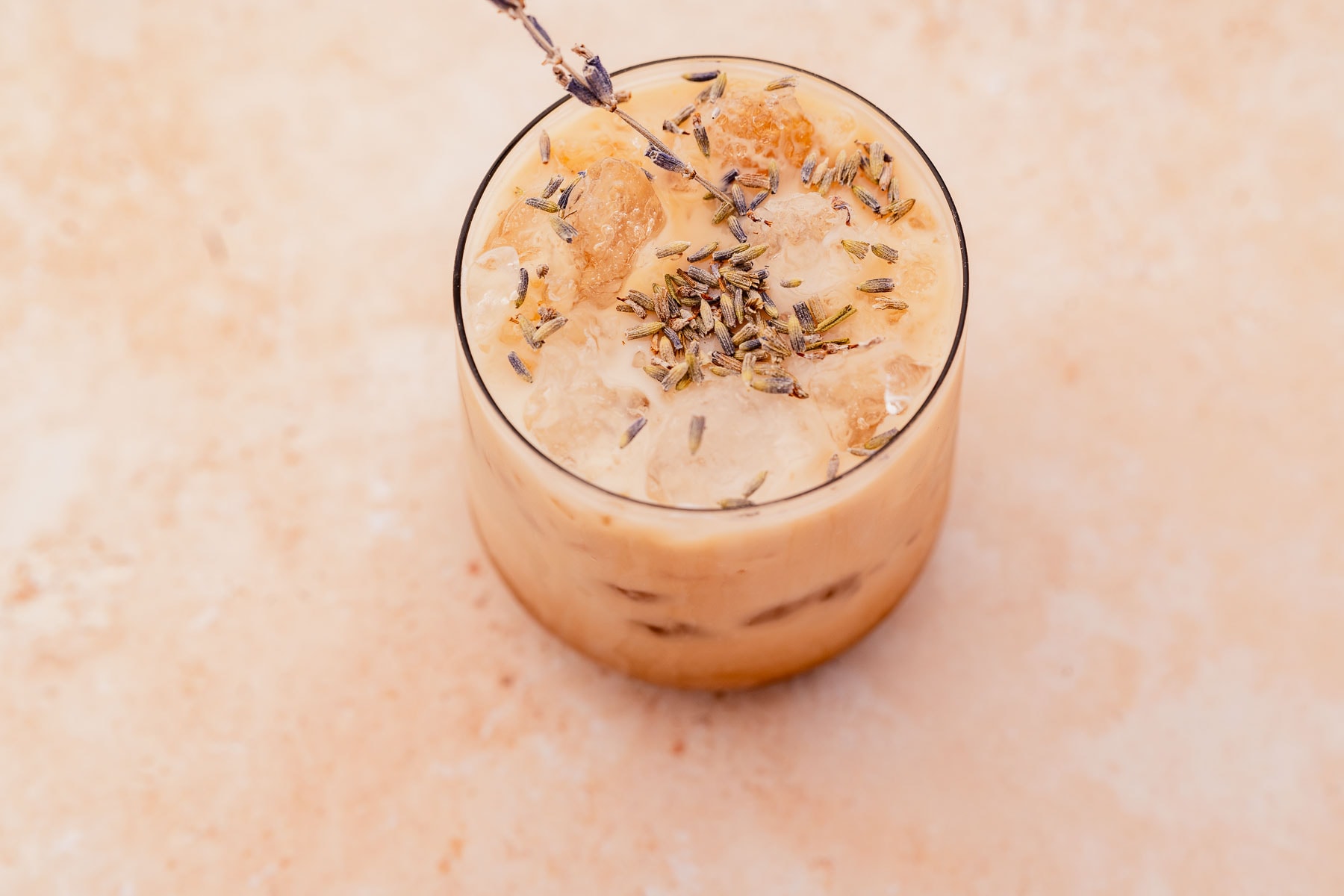 Iced lavender oatmilk latte garnished with lavender on a light-colored surface.
