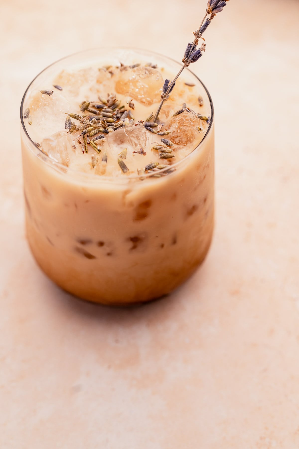 Iced Lavender Oatmilk Latte garnished with a sprig of lavender on a neutral background.