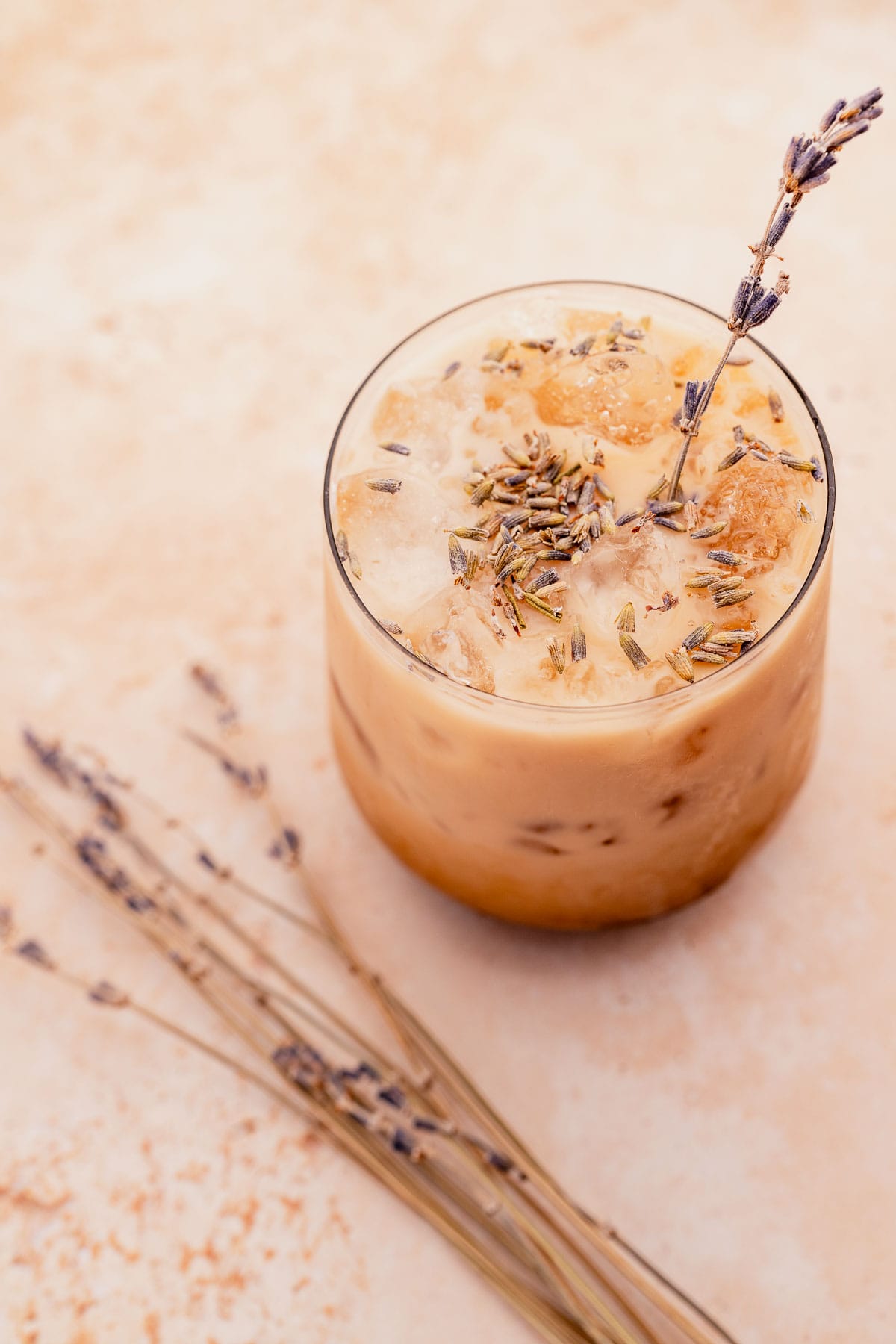 Iced lavender oatmilk latte garnished with lavender sprigs on a marble surface.