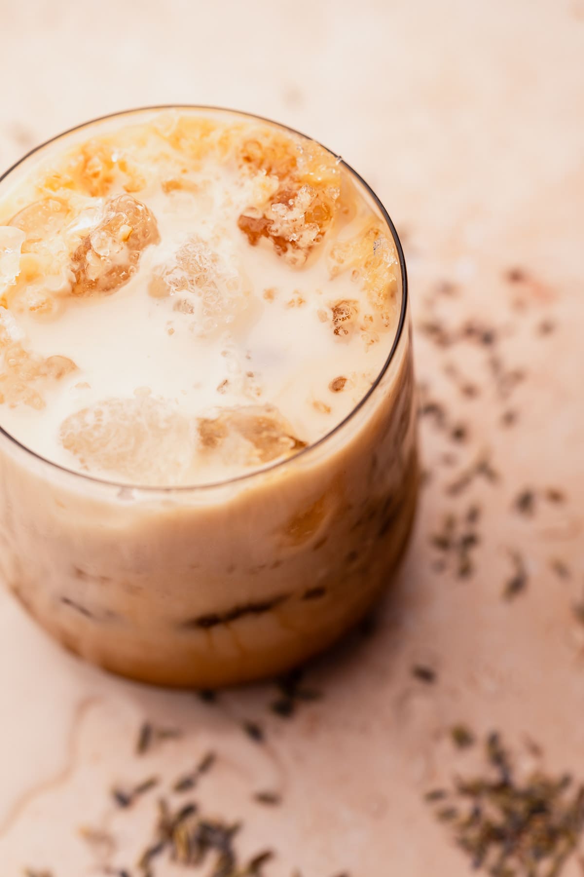 A glass of iced lavender oatmilk latte on a textured surface.