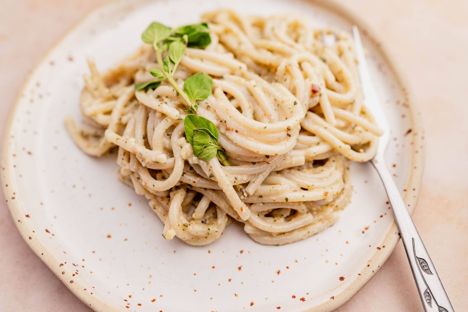 A silver fork rests on a plate of oregano pesto pasta.