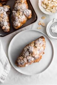 Almond croissants with powdered sugar on a plate.