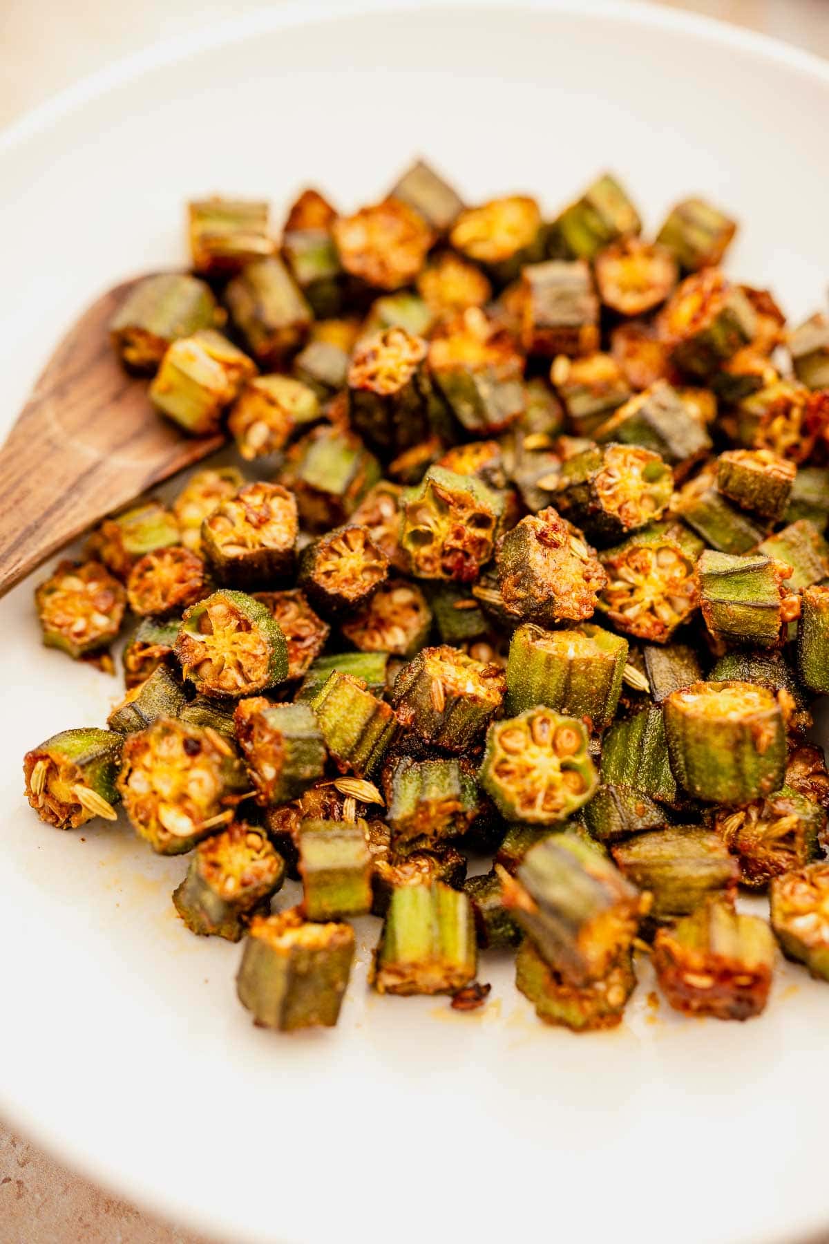 Sautéed chopped okra recipe on a white plate with a wooden spoon.