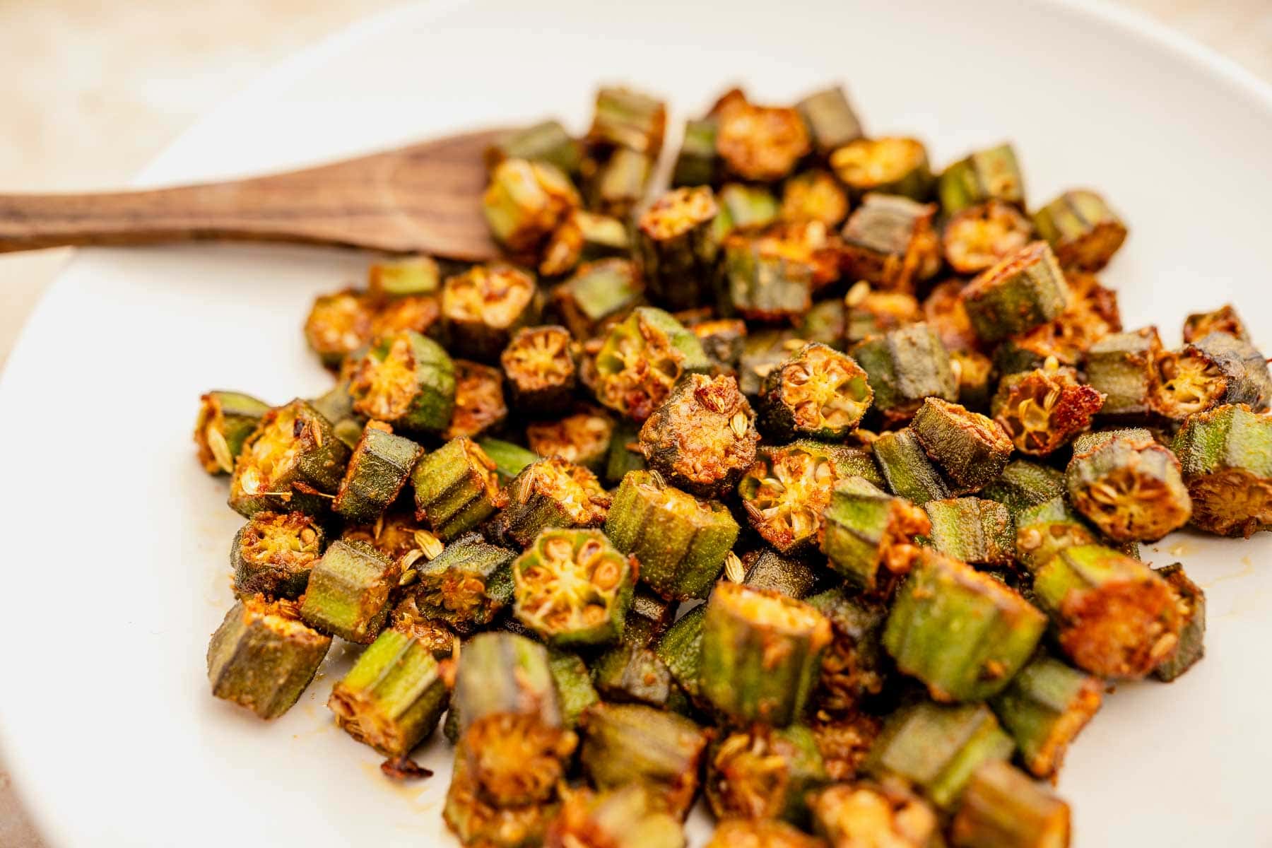 Sautéed okra recipe pieces on a white plate with a wooden fork on the side.