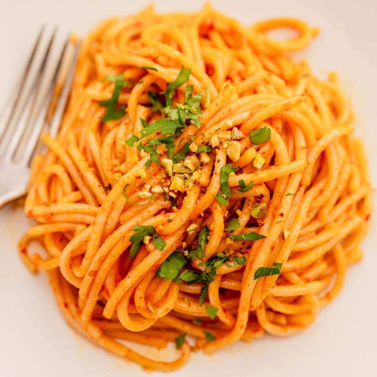 A plate of spaghetti garnished with chopped herbs and nuts, accompanied by a fork on the side.