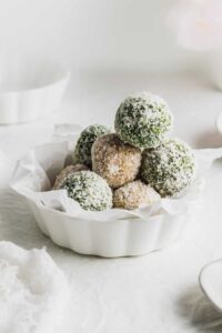 A white bowl filled with green balls on a white table.