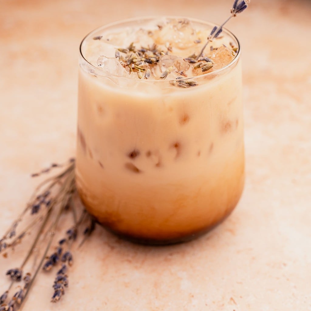Iced lavender oatmilk latte in a glass with a sprig of lavender garnish.