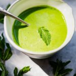 A bowl of vibrant green soup garnished with a yogurt mint chutney.