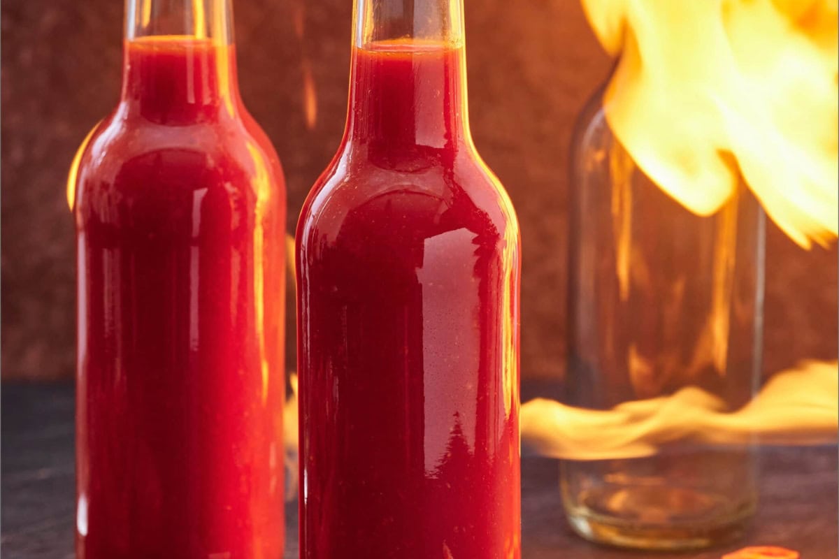 Two bottles of red hot sauce with a fiery flame in the background, emphasizing the sauce's spiciness.