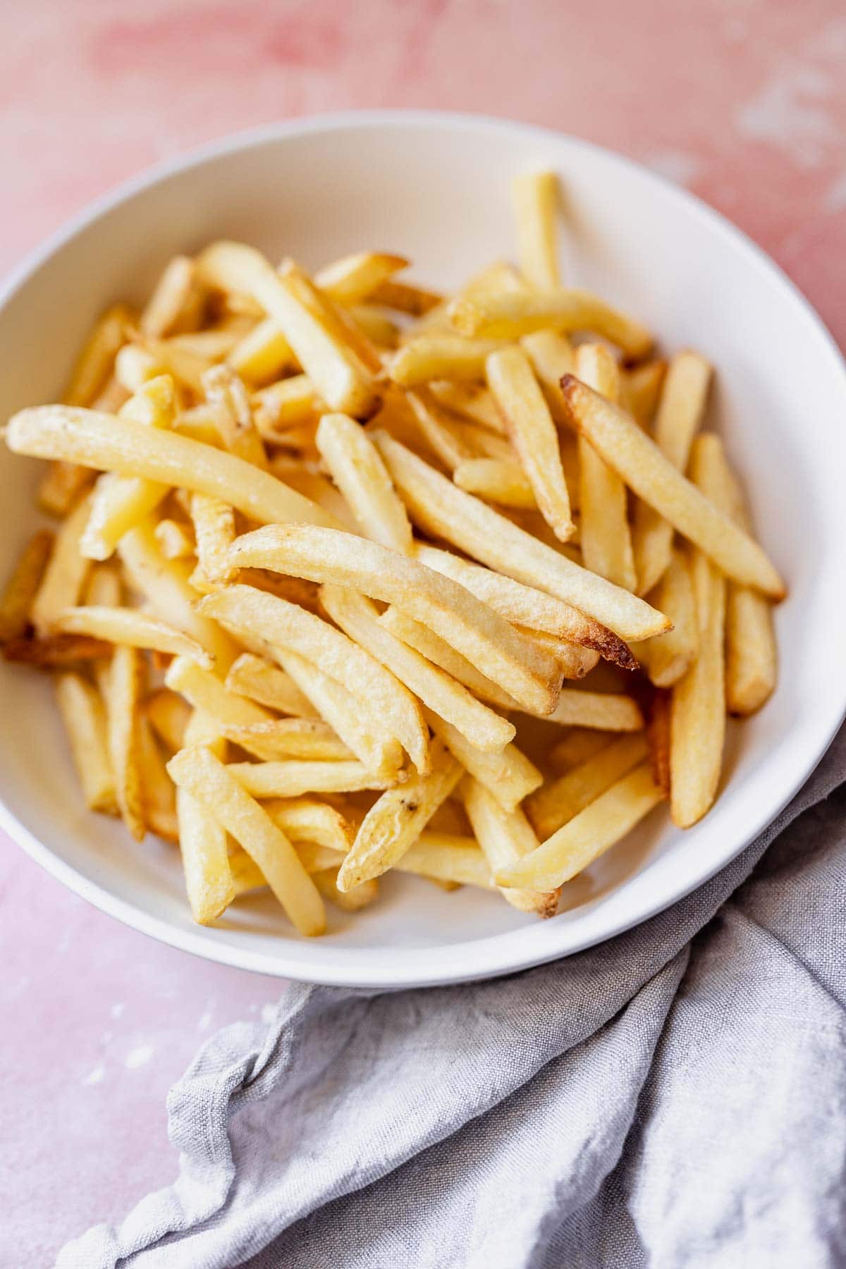 Bowl of crispy golden air fryer french fries on a light background.