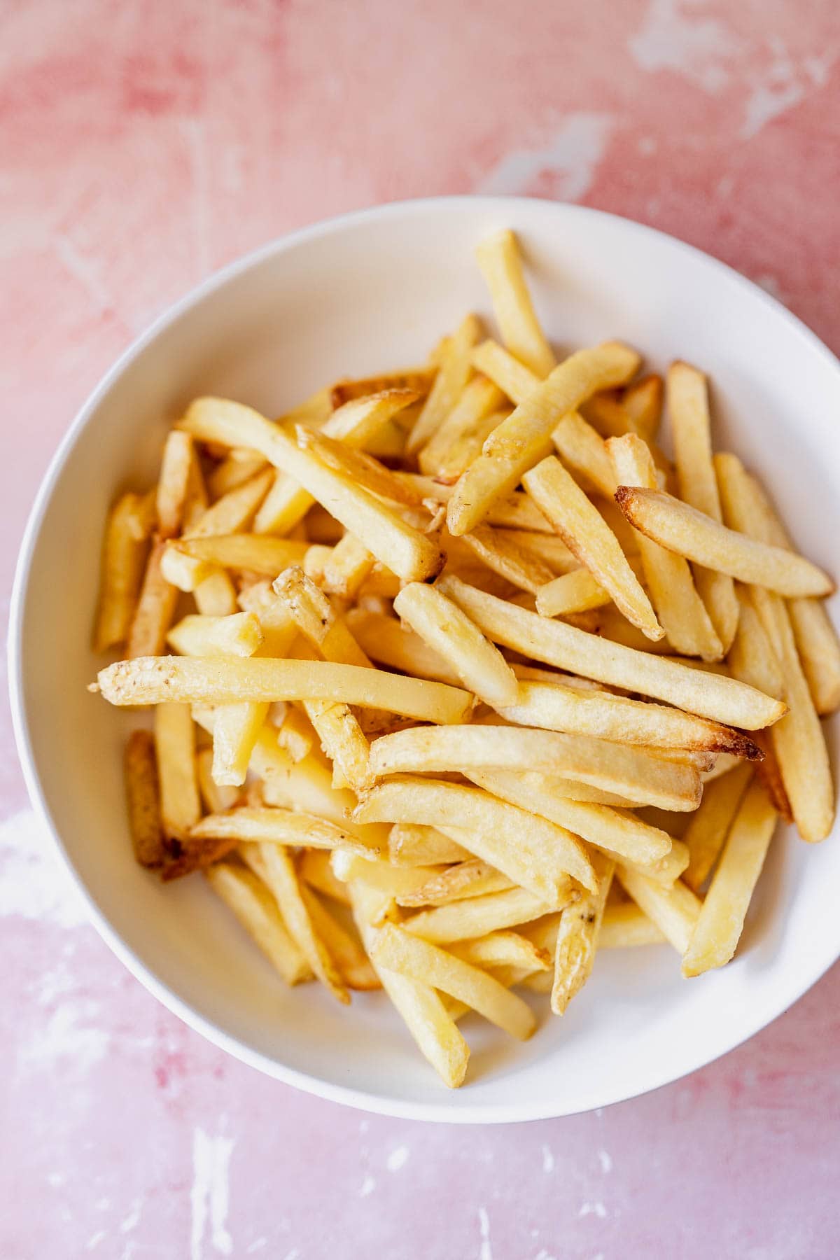 A bowl of golden air fryer frozen french fries on a pink surface.