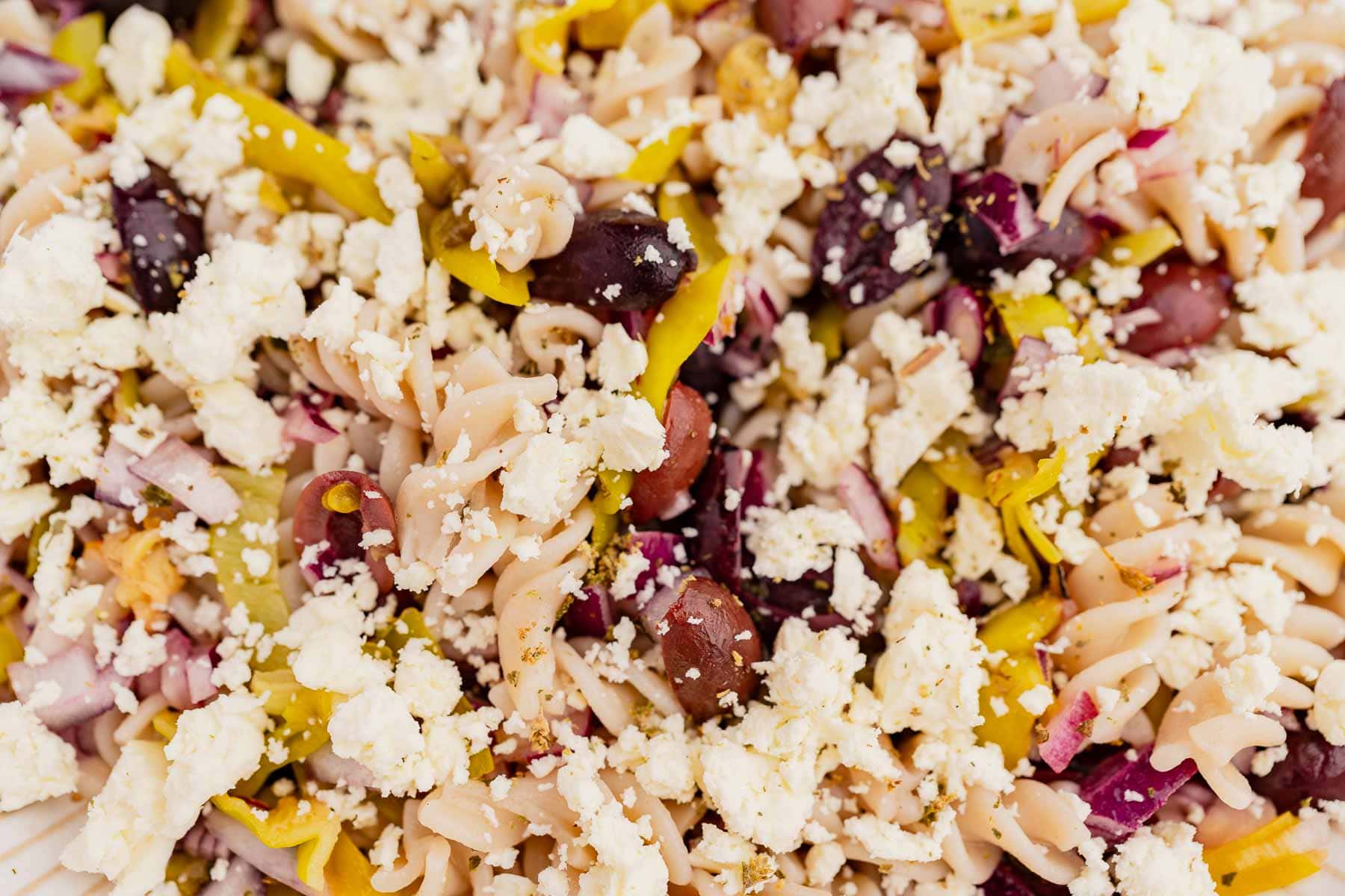 Close-up of a Greek pasta salad with olives, red onions, feta cheese, and yellow peppers.