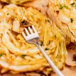 Roasted cabbage steaks with a fork digging into one of the cabbage steaks, garnished with herbs.
