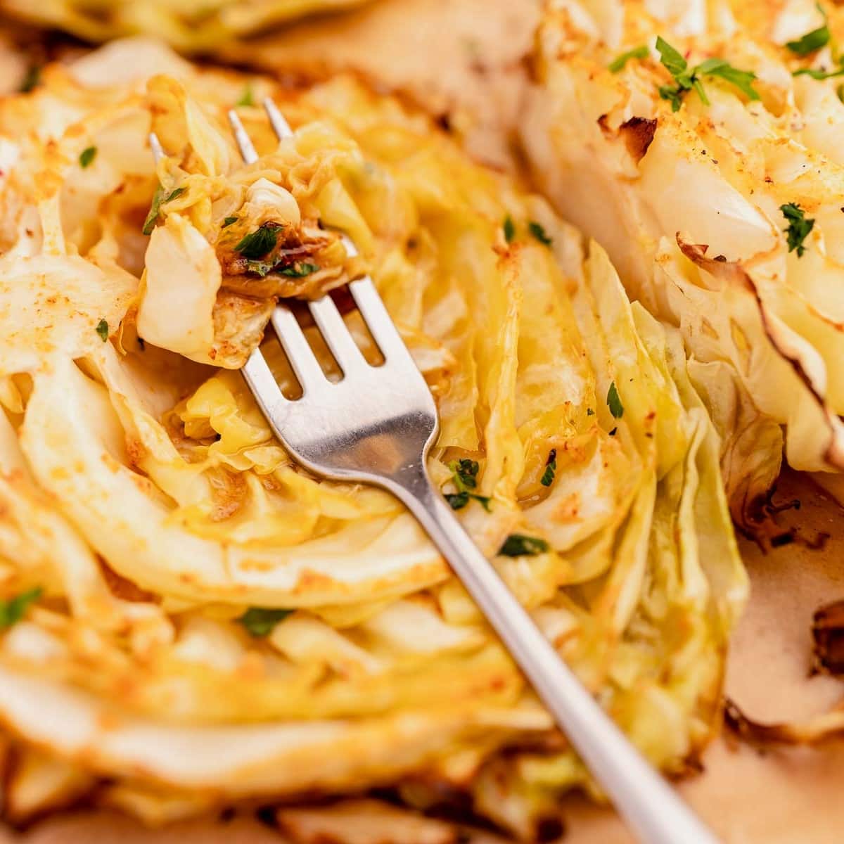 Roasted cabbage steaks with a fork digging into one of the cabbage steaks, garnished with herbs.