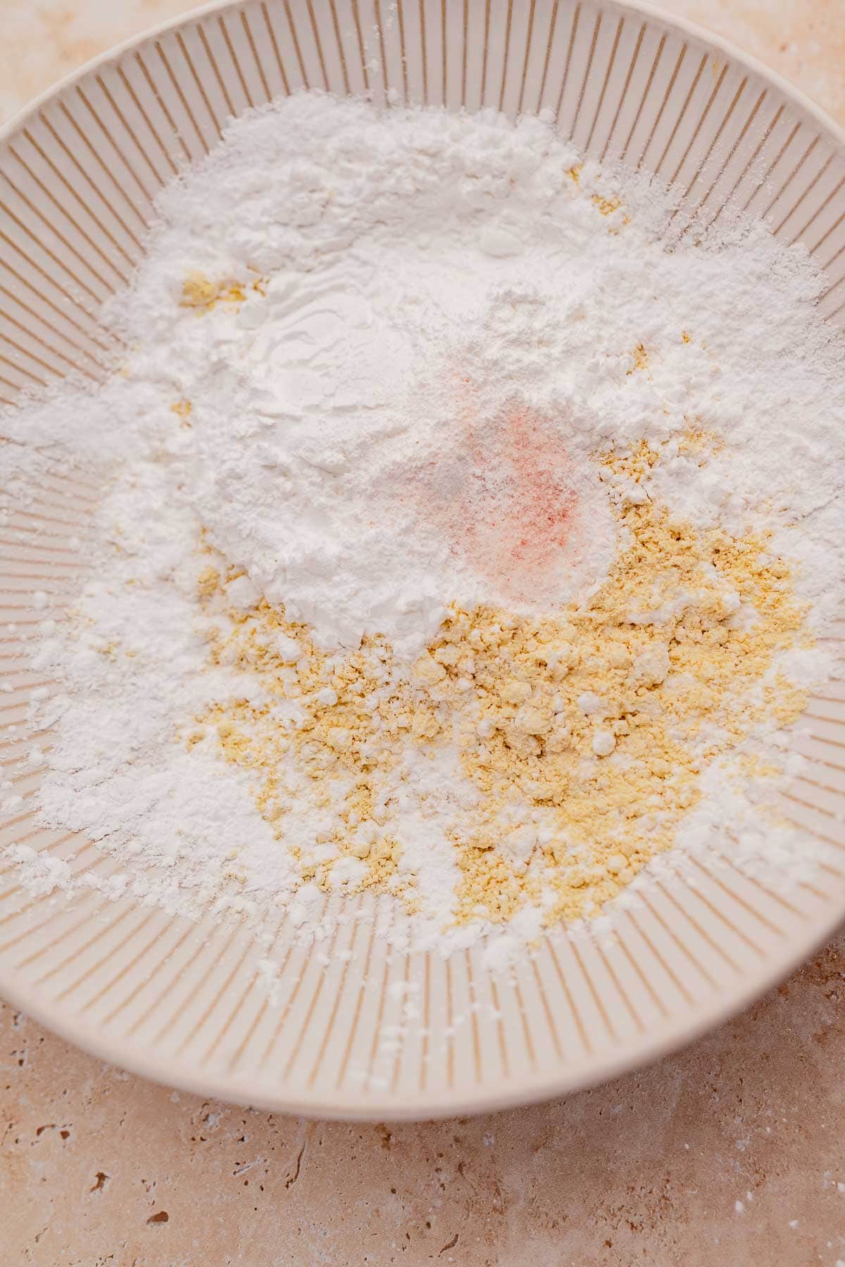 A bowl containing a mix of chickpea flour, baking powder, and a pinch of salt on a kitchen counter.