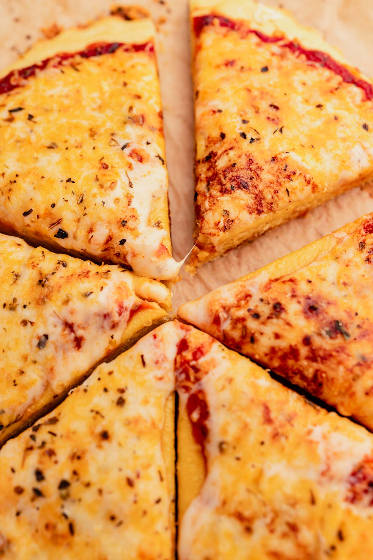 Slices of cheese pizza with a chickpea flour crust, featuring a visible melted cheese pull on a wooden surface.