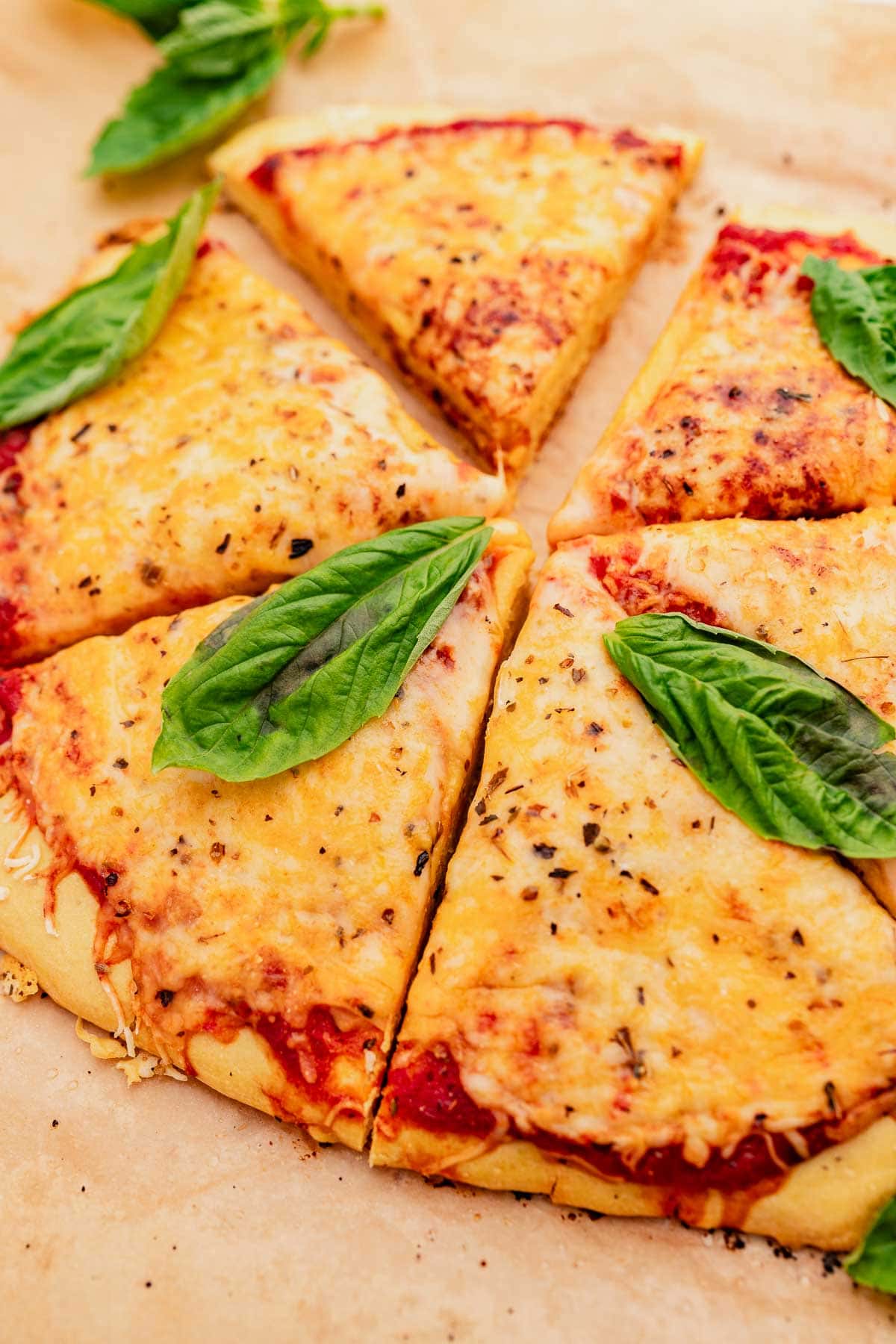 Sliced cheese pizza with a chickpea flour crust, topped with fresh basil leaves.
