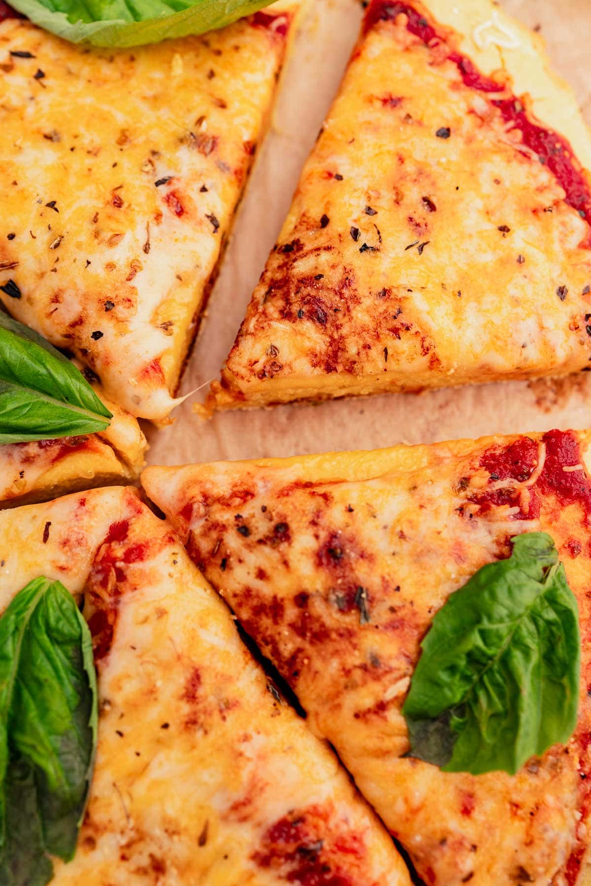 Close-up of sliced margherita pizza with chickpea flour crust, garnished with fresh basil leaves and lime wedges.