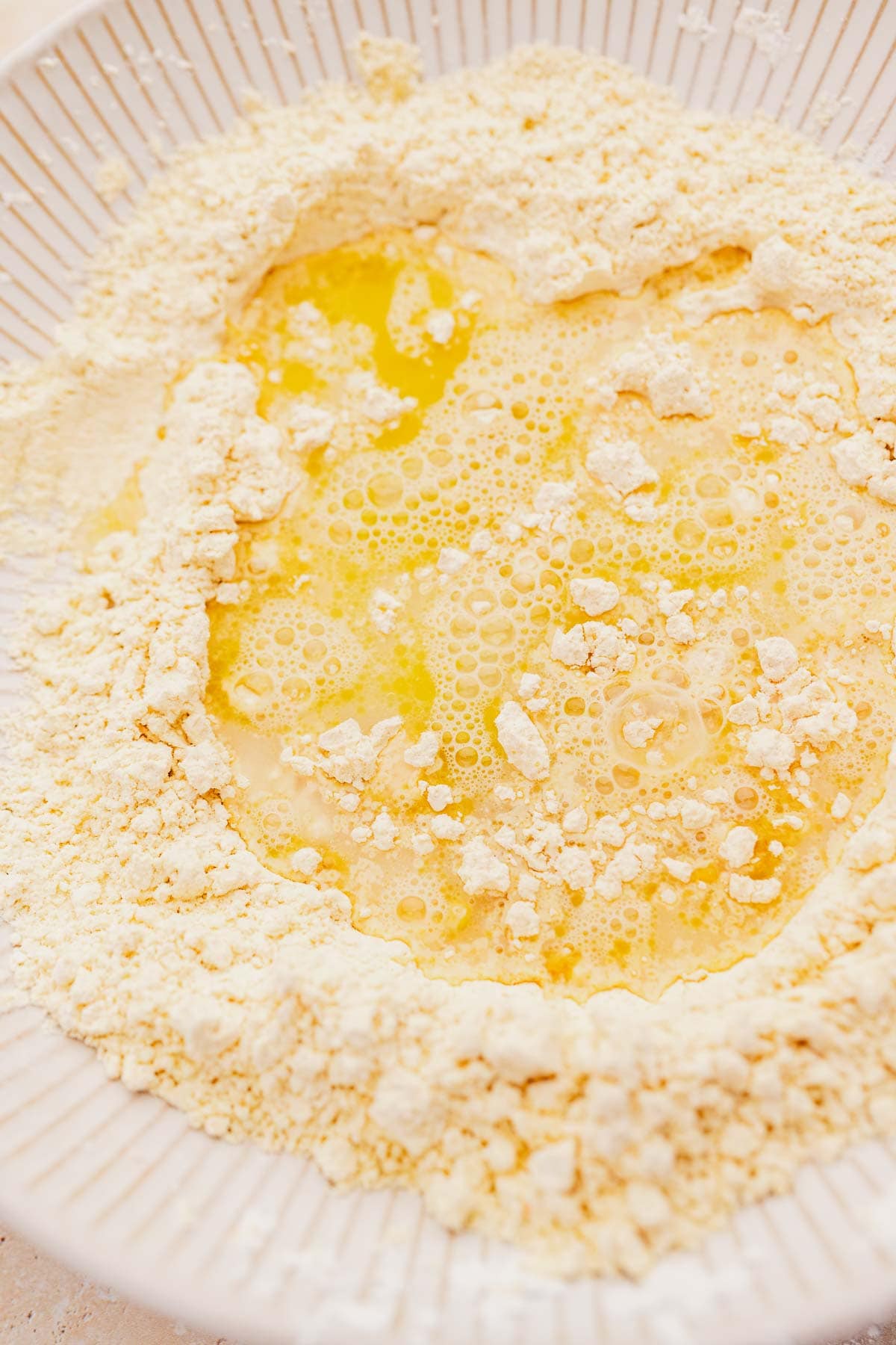 Melted butter mixing with chickpea flour in a white bowl, showing the beginning stages of pizza crust preparation.