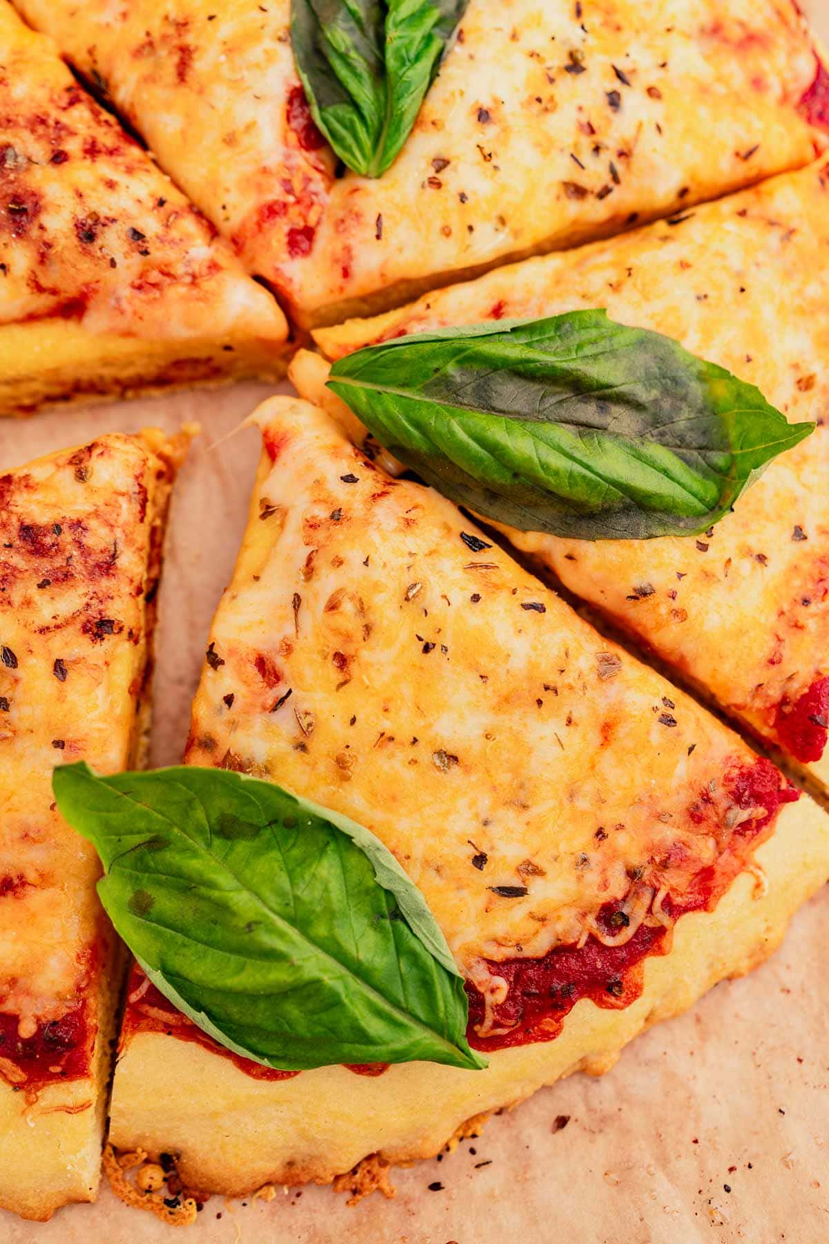 Sliced cheese pizza with fresh basil leaves on top, served on a chickpea flour pizza crust and a wooden surface.