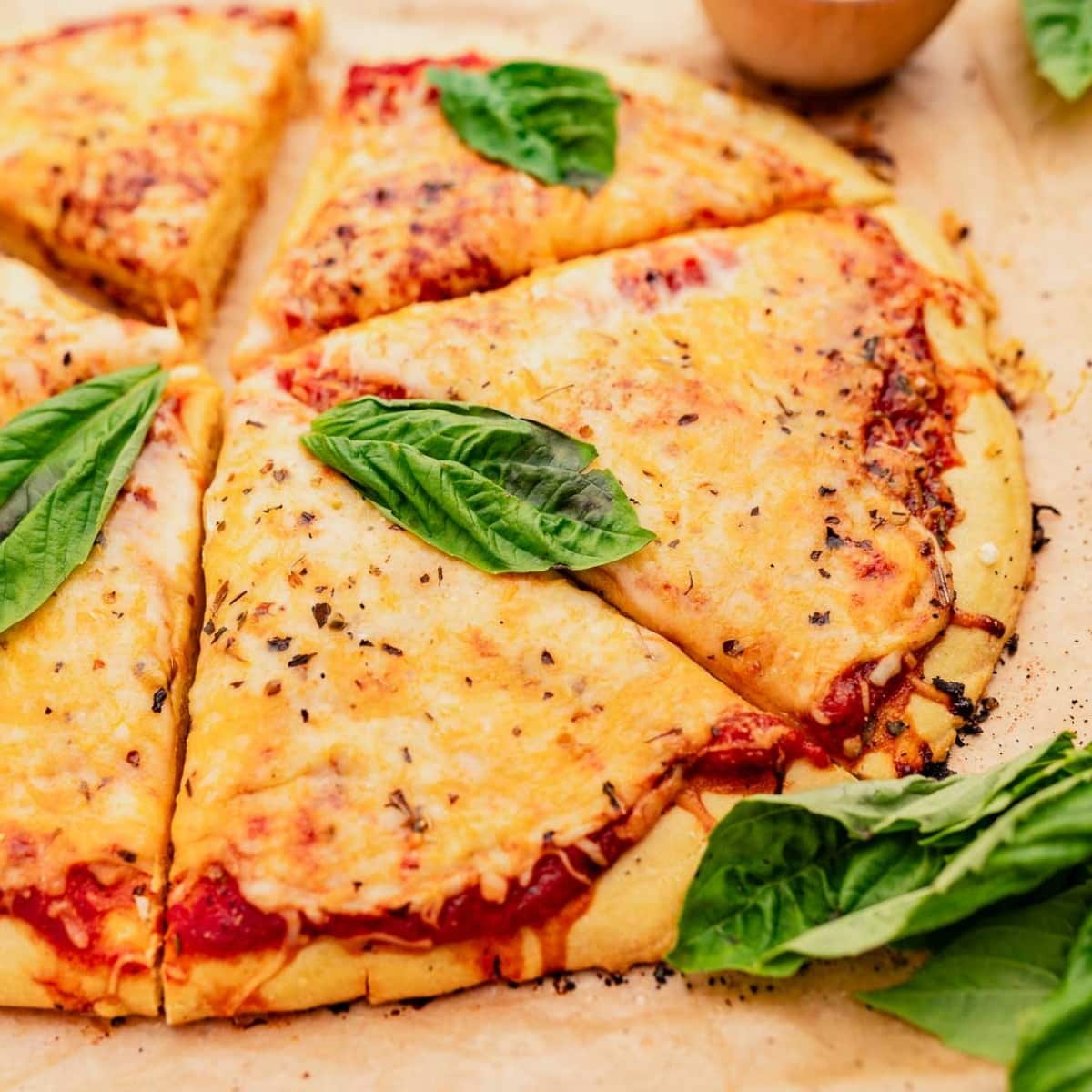 A close-up of a sliced cheese pizza with a chickpea flour crust, garnished with fresh basil leaves on a light surface.