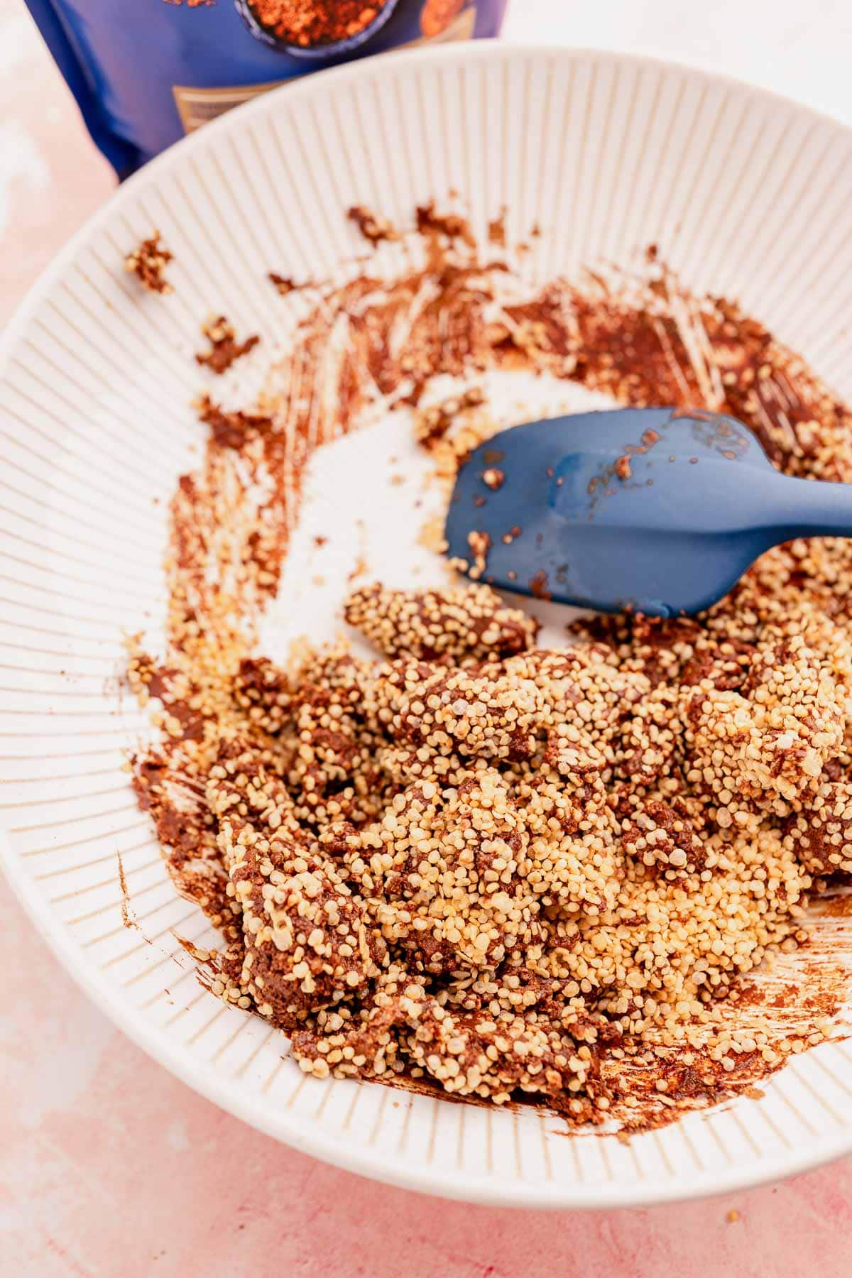 Bowl with mixed ingredients including chocolate crumbs and quinoa crunch bites, with a blue spatula.