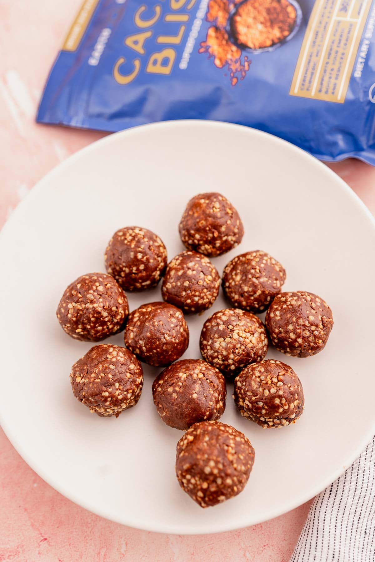 Quinoa crunch bites arranged on a white plate, with a bag of cacao nibs partially visible in the background.