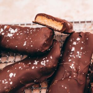 Chocolate-covered high-protein candy bars with a caramel middle, sprinkled with salt, arranged on a metal cooling rack.