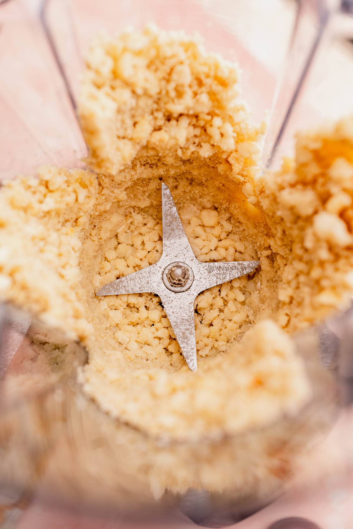 Crushed macadamia nut butter and cookie crumbs in a blender with a visible metal blade.