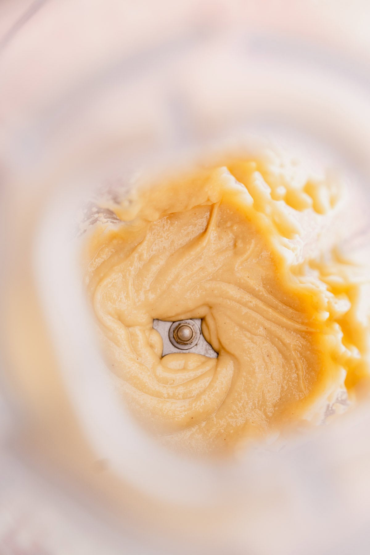 Close-up of macadamia nut butter being blended in a food processor, focusing on the swirling texture and blade.
