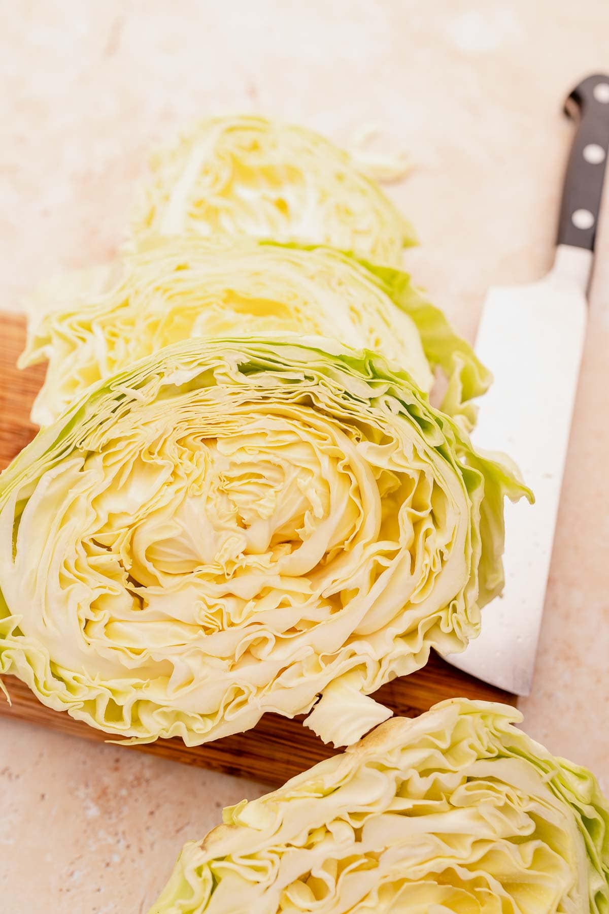 Sliced cabbage steaks on a wooden cutting board next to a chef's knife, showcasing the layered interior of the vegetable.