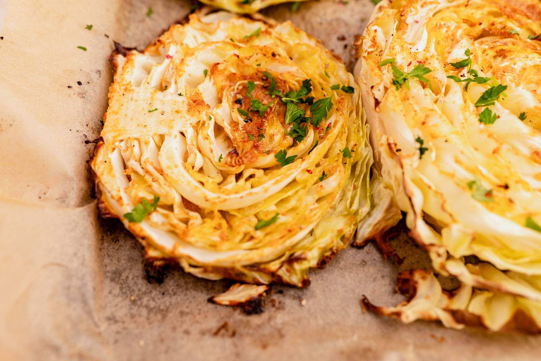 Roasted cabbage steaks seasoned with spices and garnished with parsley on parchment paper.