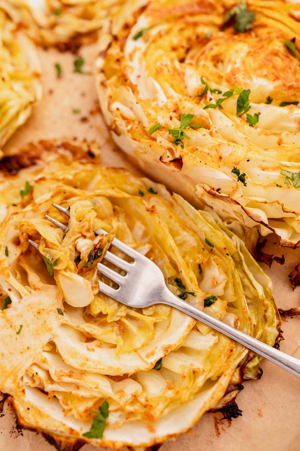 Sliced roasted cabbage steaks garnished with parsley, with a fork on one piece, on parchment paper.
