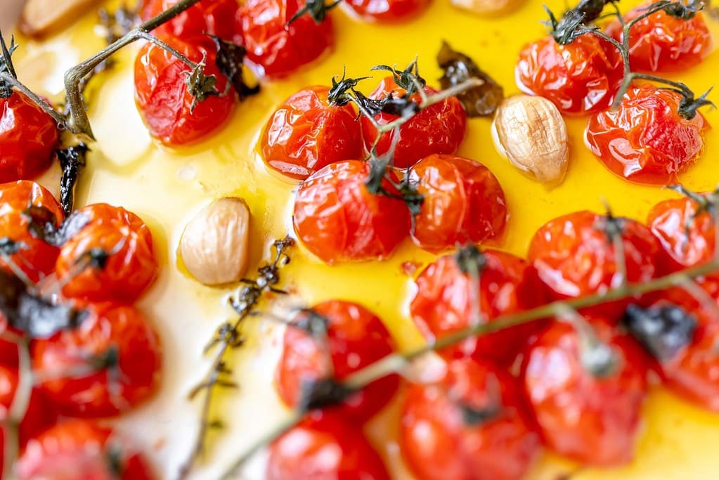 Close-up of roasted cherry tomatoes and garlic cloves on the vine, surrounded by a yellow sauce, perfect as side dishes.