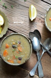 Three bowls of slow-cooked mixed vegetable soup served on a rustic wooden table, with lemon slices and vintage spoons nearby.