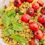 A plate of vibrant pesto rice topped with roasted cherry tomatoes and garnished with fresh basil leaves.