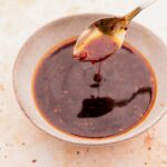 A spoon dripping Korean BBQ sauce over a bowl filled with chili oil.