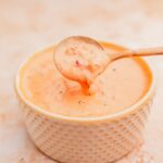 A spoon scooping a creamy Algerian sauce from a white textured bowl.