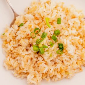 A plate of garlic fried rice garnished with chopped green onions, with a fork resting on the side.