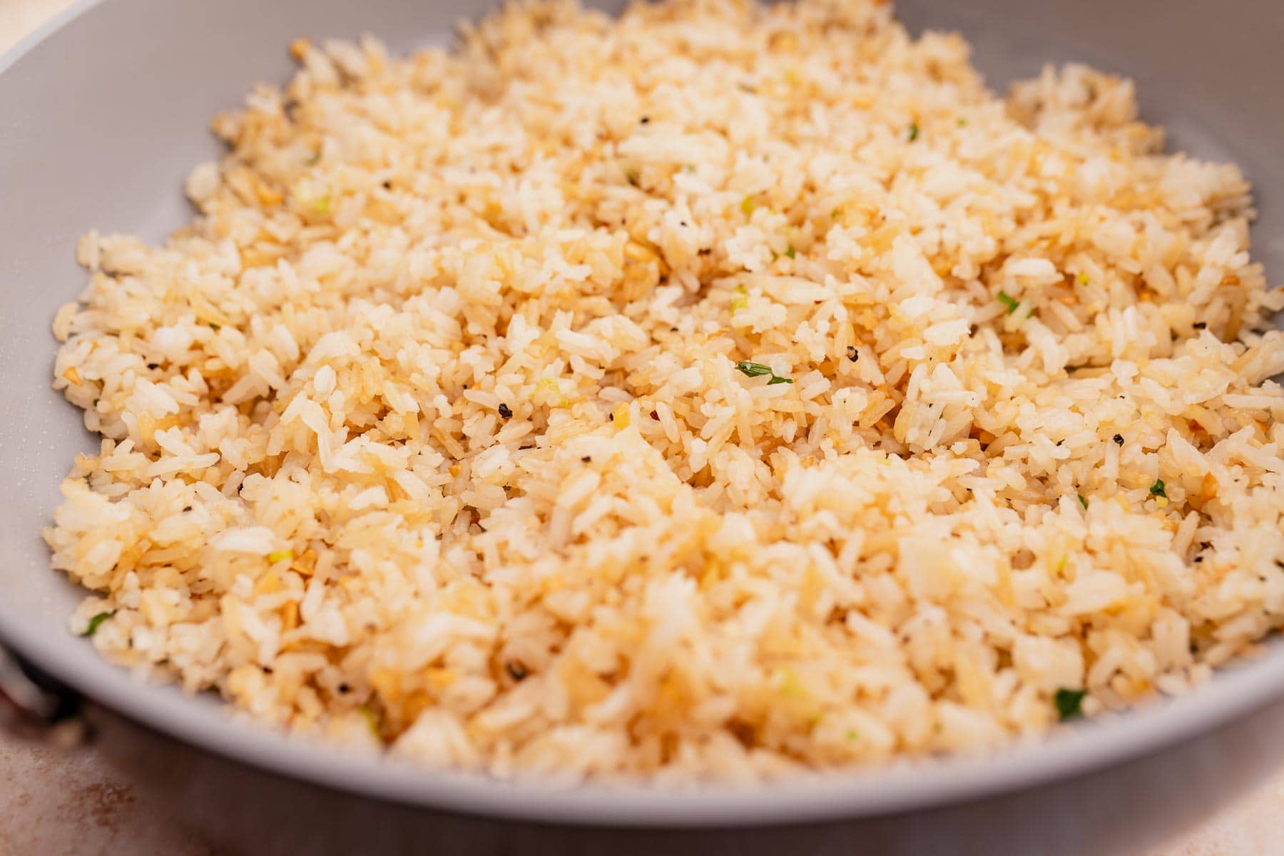 A close-up of a bowl filled with garlic fried rice, showcasing grains mixed with small bits of vegetables and light seasoning.