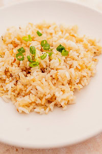 A white plate with a serving of garlic fried rice, garnished with chopped green onions.