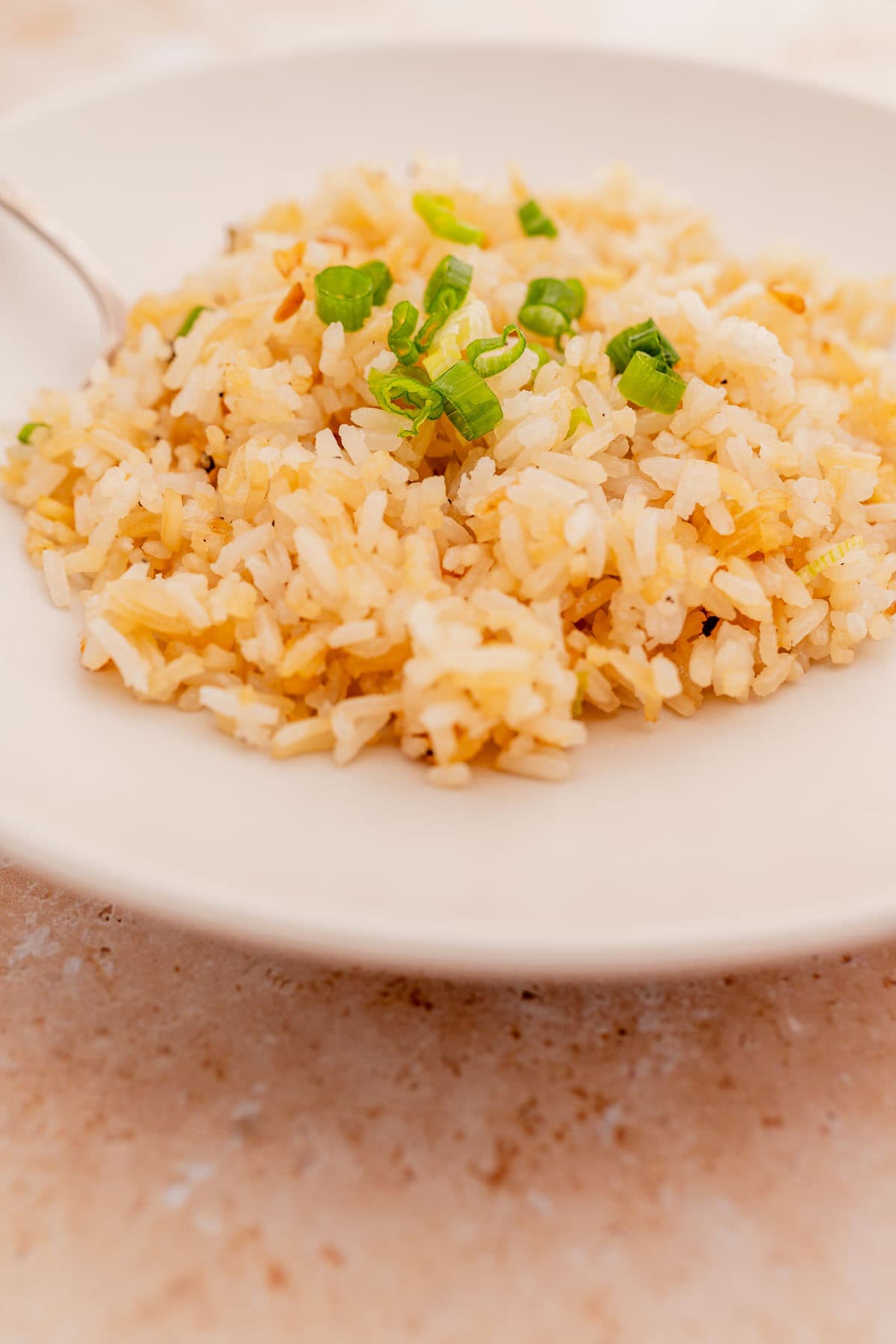 A plate of garlic fried rice garnished with chopped green onions, served on a light-colored, round ceramic plate.