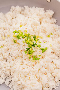 A close-up of a bowl of garlic fried rice garnished with chopped green onions.