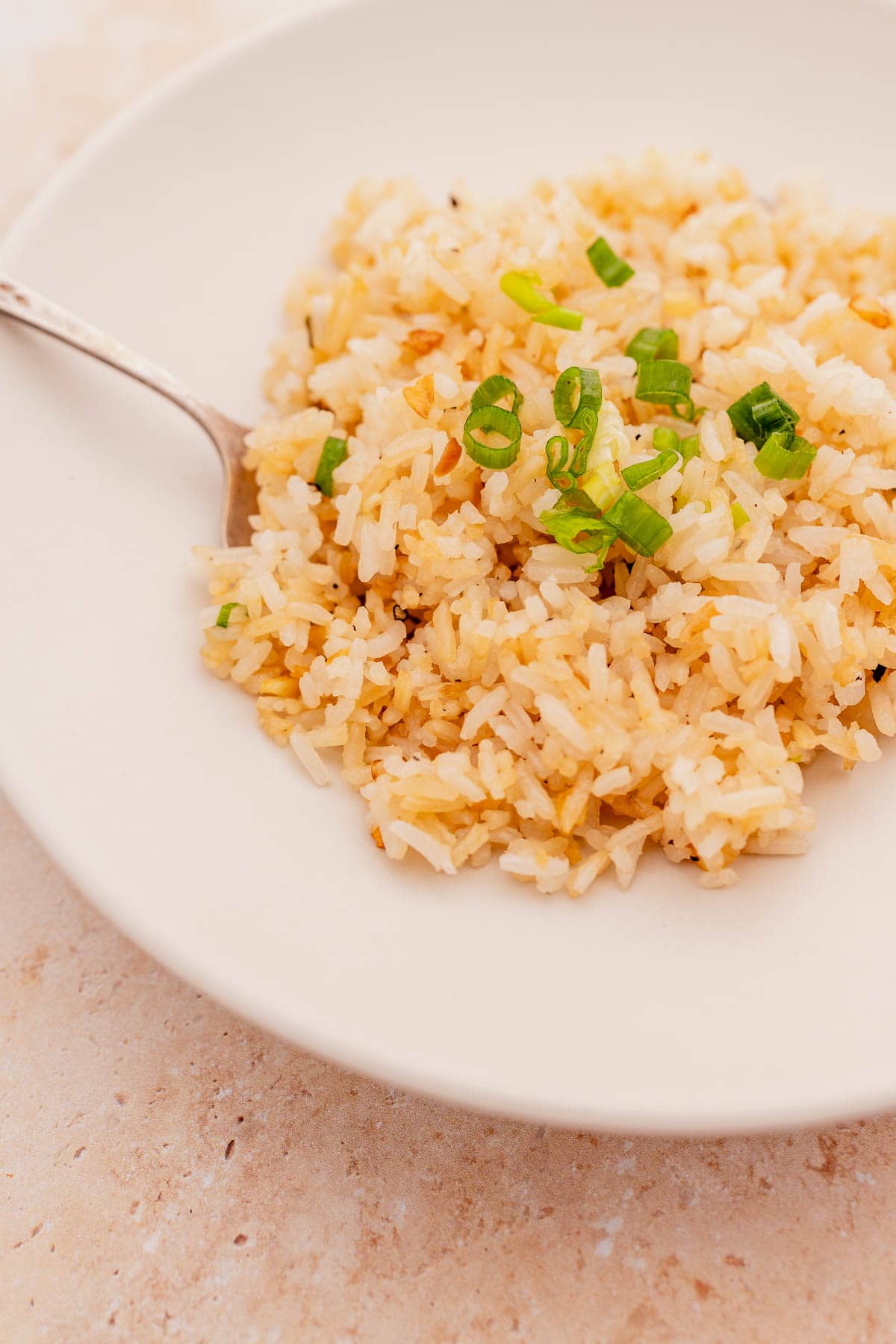 A plate of garlic fried rice garnished with chopped green onions, with a spoon resting on the edge.