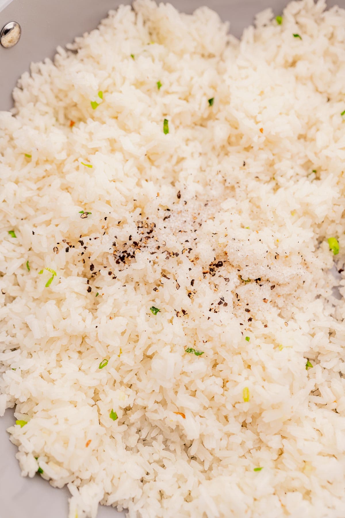 A close-up of garlic fried rice mixed with small green herbs and sprinkled with black pepper.