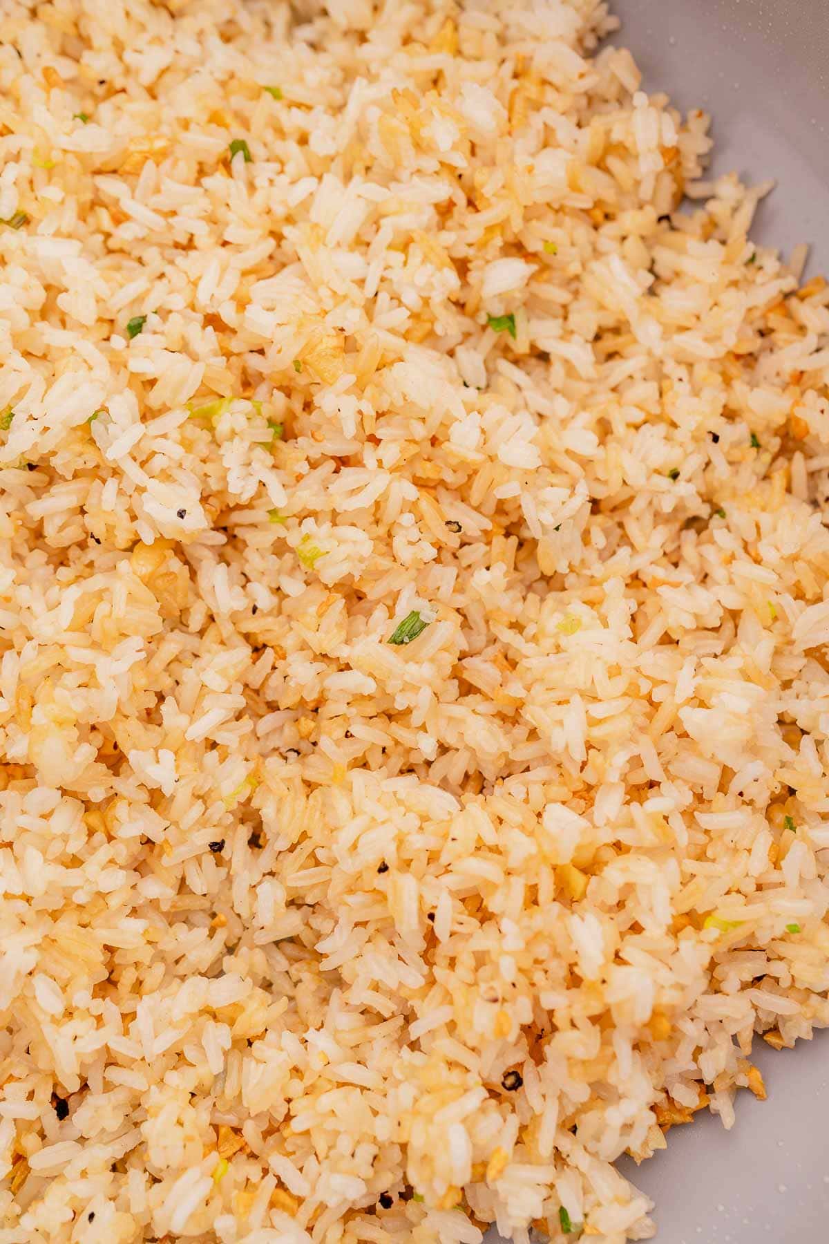 Close-up of a plate of garlic fried rice with visible bits of vegetables and seasonings.